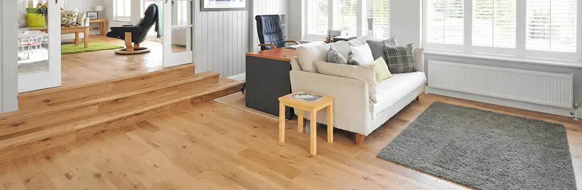 A modern living room with professionally installed laminate flooring, a beige sofa, a small side table, a gray rug, and large windows with white shutters in Birmingham, AL